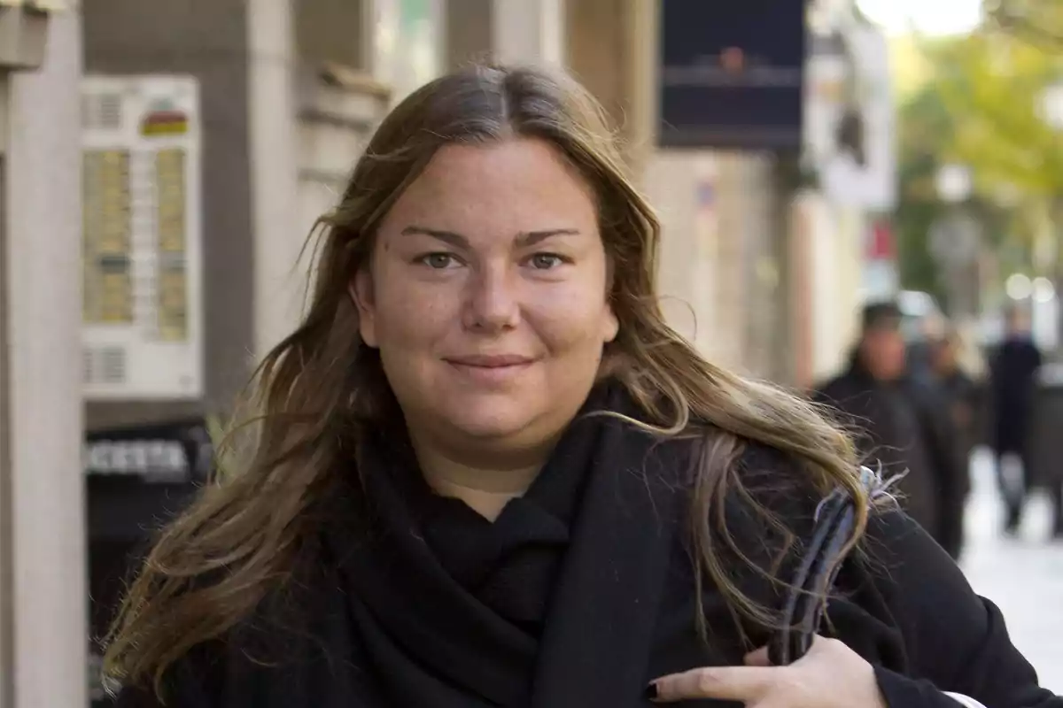 Una mujer con cabello largo y suelto, vestida con ropa oscura, caminando por una calle urbana.