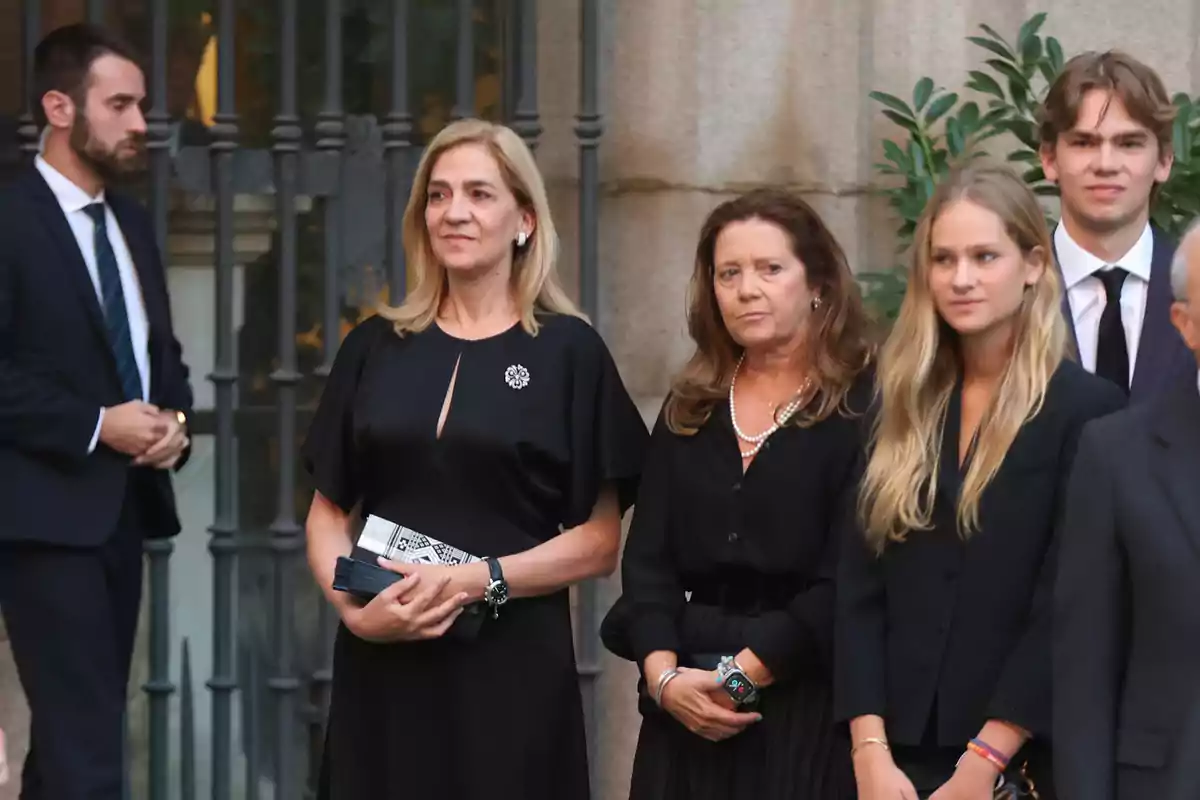 Varias personas vestidas de negro posan juntas en un evento formal al aire libre frente a una puerta de hierro y una pared de piedra Varias personas vestidas de negro posan juntas en un evento formal al aire libre frente a una puerta de hierro y una pared de piedra