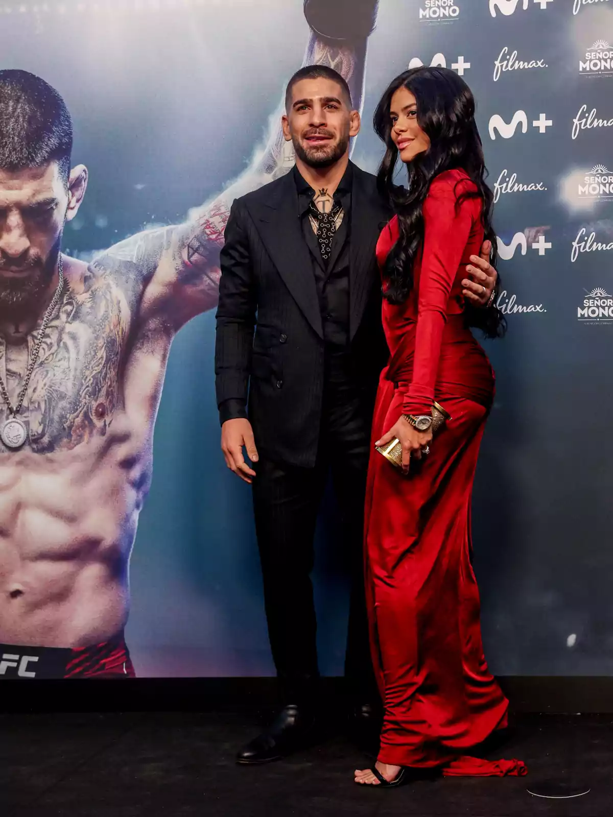 Una pareja posando en un evento con un fondo promocional de una película o serie.