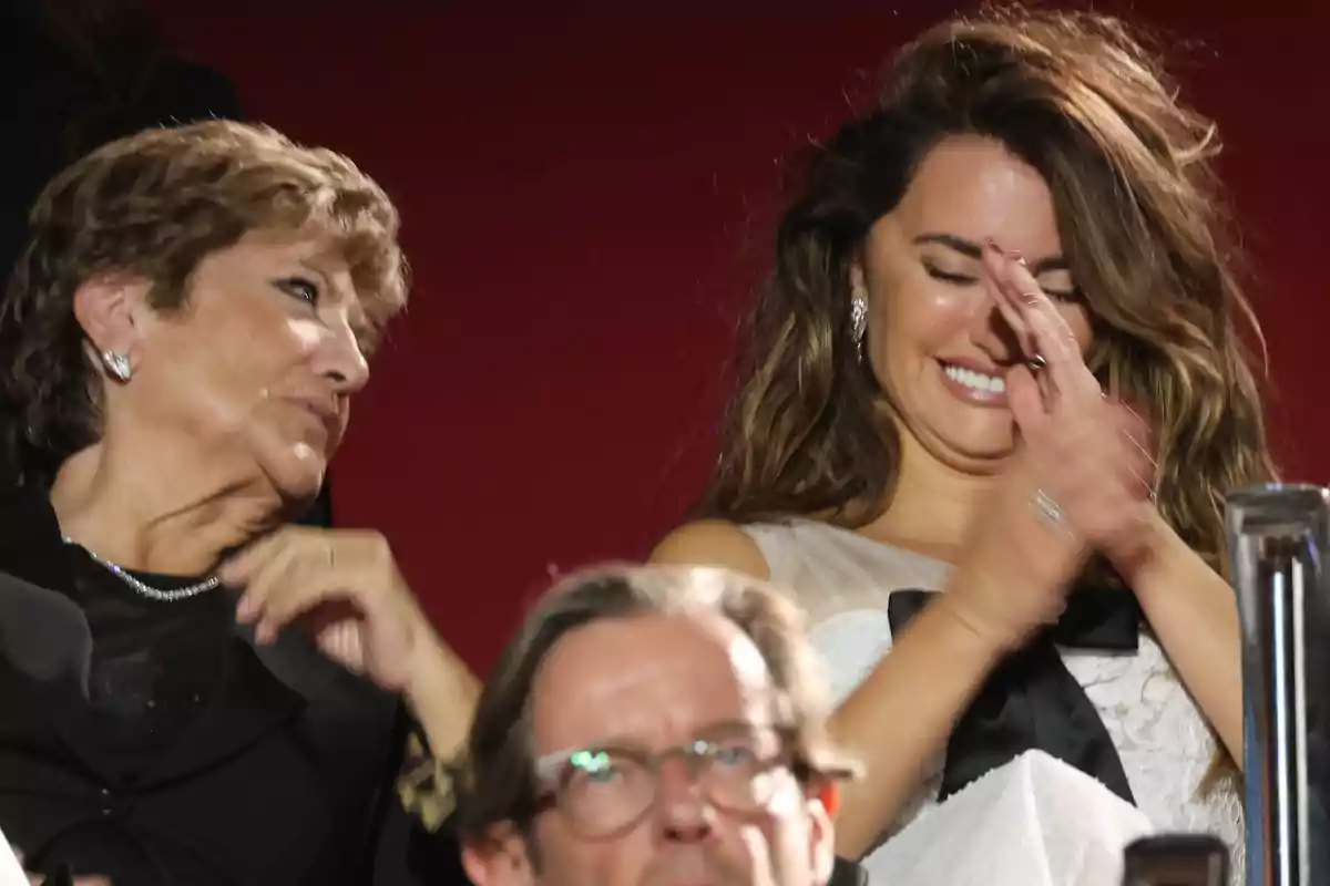 Dos personas sentadas en un evento, una de ellas aplaudiendo y sonriendo. Dos personas sentadas en un evento, una de ellas aplaudiendo y sonriendo.