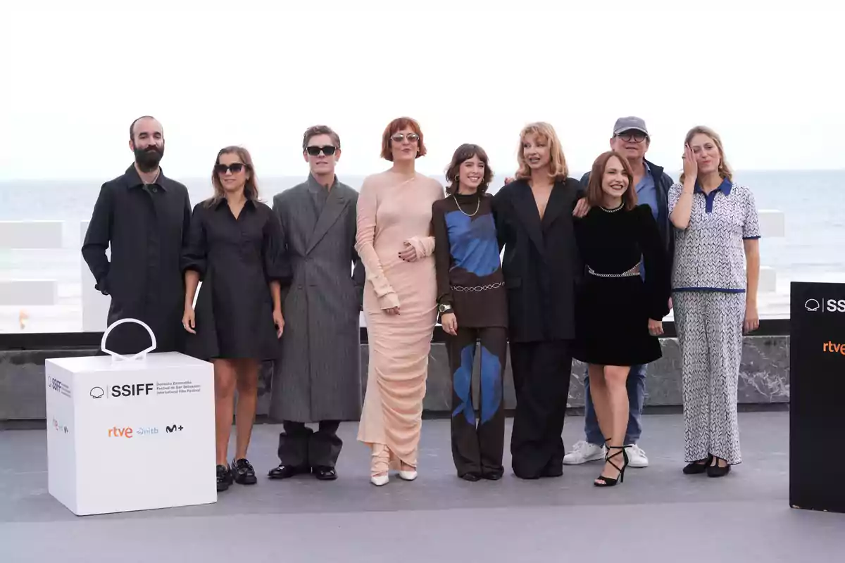 Un grupo de personas posando en un evento al aire libre junto al mar, con un cartel del Festival Internacional de Cine de San Sebastián.