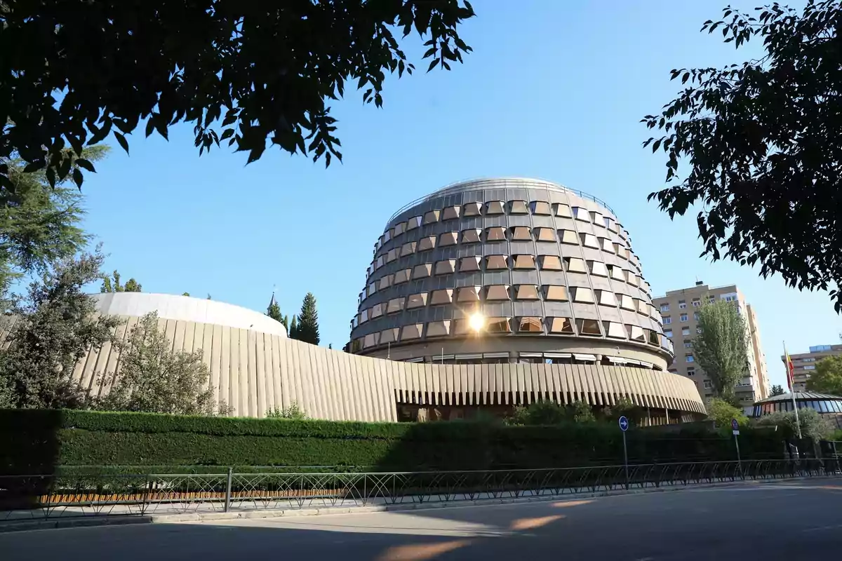 Edificio moderno con diseño circular y ventanas geométricas rodeado de vegetación y árboles bajo un cielo despejado. Edificio moderno con diseño circular y ventanas geométricas rodeado de vegetación y árboles bajo un cielo despejado.