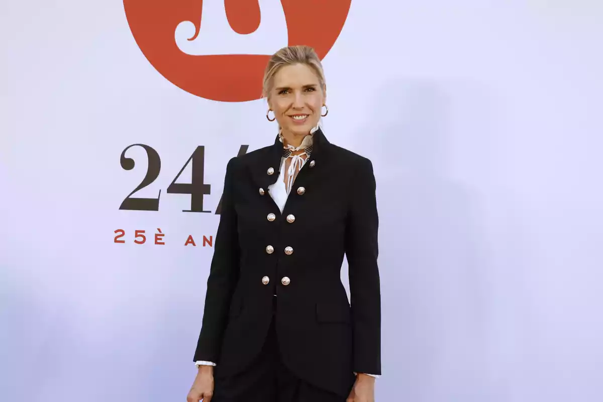Una persona con un traje negro elegante posando frente a un fondo blanco con un logotipo rojo y texto que dice "25è ANIVERSAIRE".