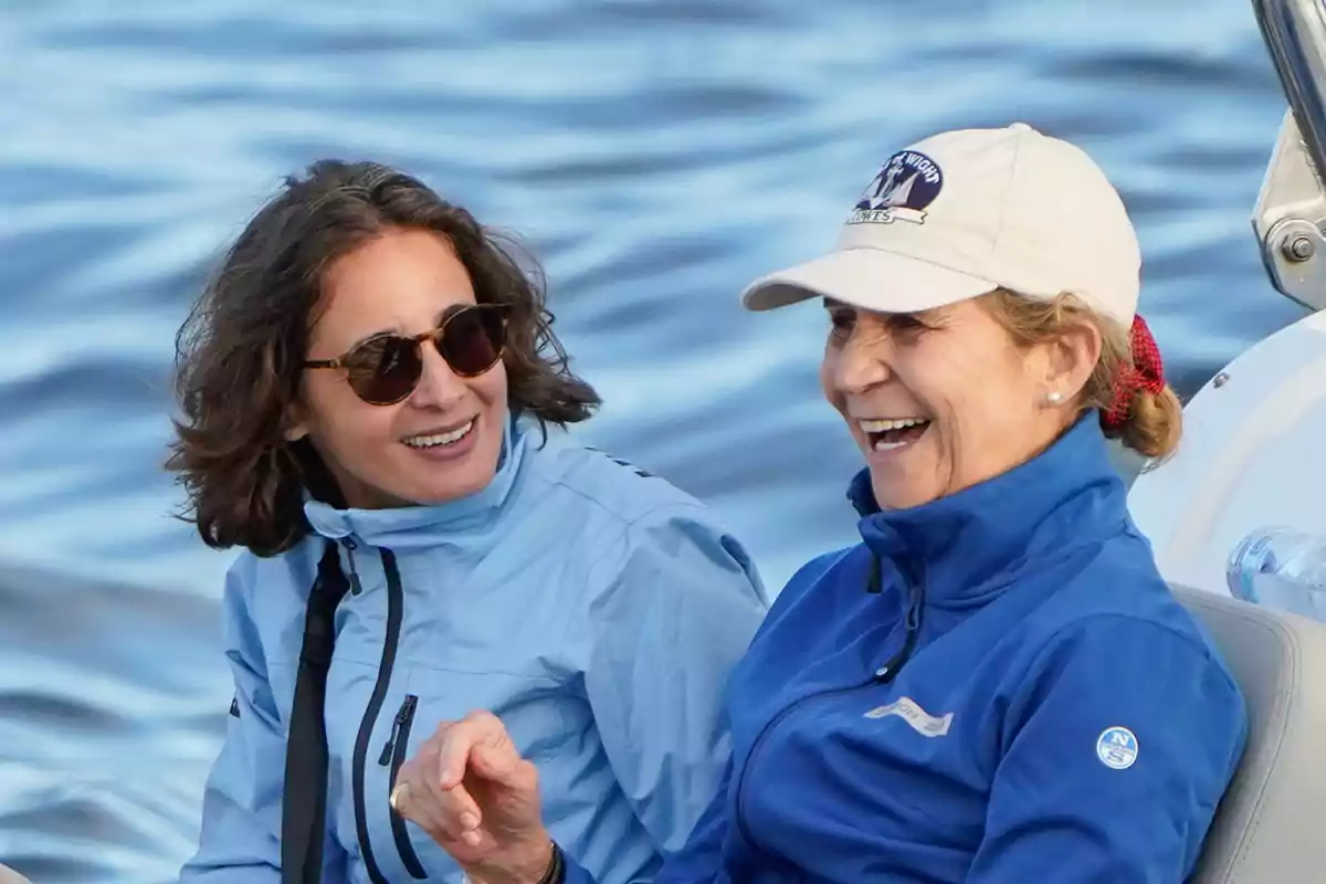 Dos personas sonrientes con chaquetas azules y gafas de sol disfrutan de un paseo en bote sobre el agua.