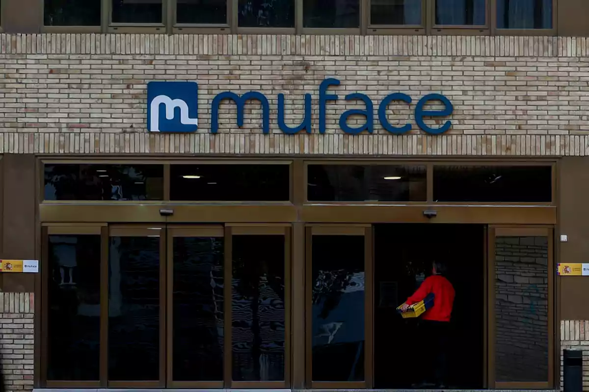 Fachada de un edificio de ladrillo con el logo de Muface sobre la entrada principal y una persona entrando por la puerta.