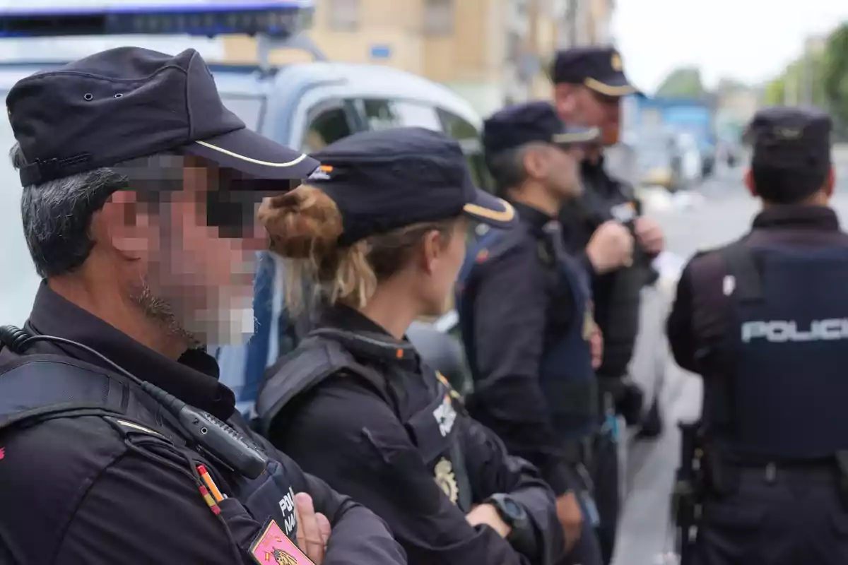 Varios agentes de policía con uniforme y chaleco antibalas están de pie junto a un vehículo patrulla en una calle