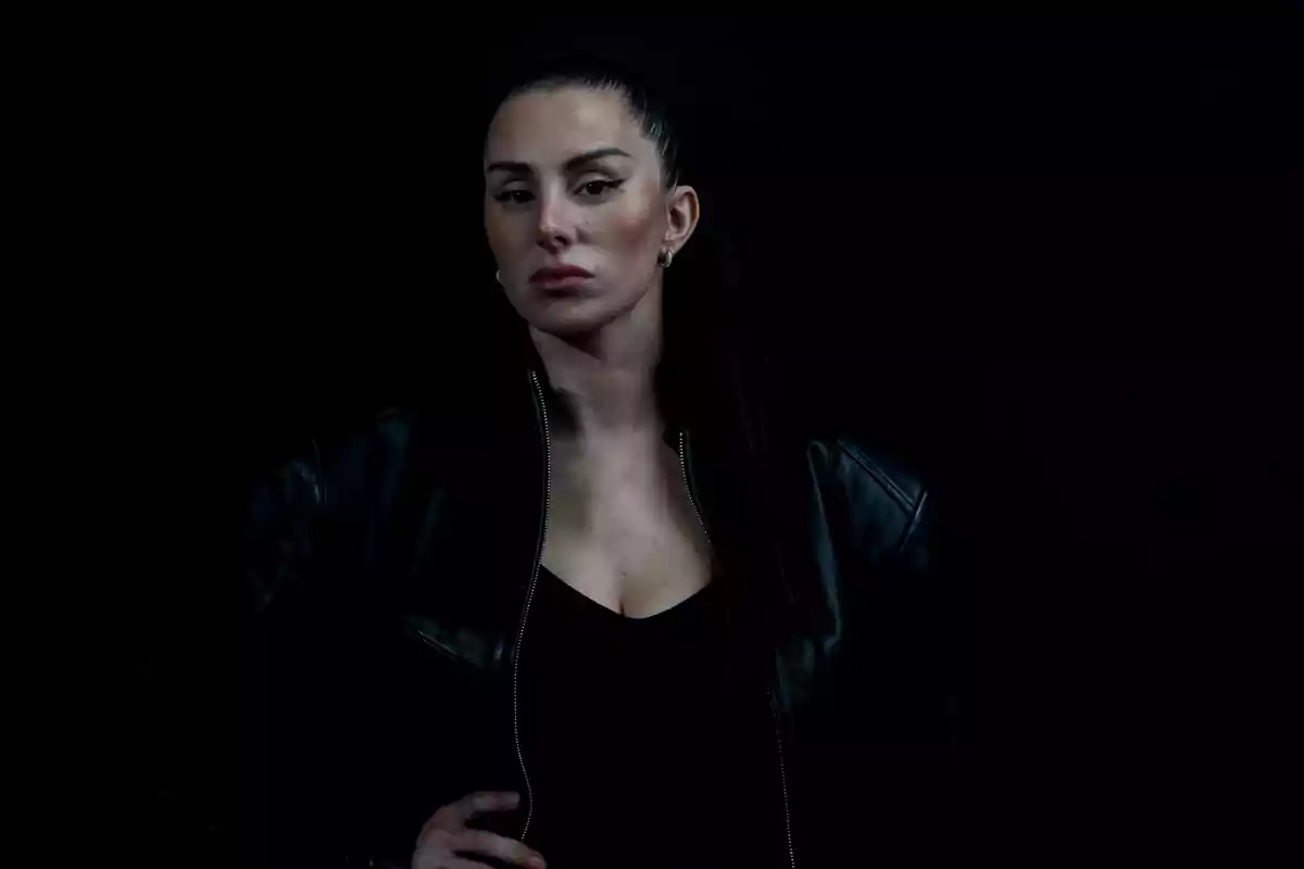 Mujer de cabello oscuro recogido con chaqueta de cuero negro posando sobre un fondo oscuro Mujer de cabello oscuro recogido con chaqueta de cuero negro posando sobre un fondo oscuro
