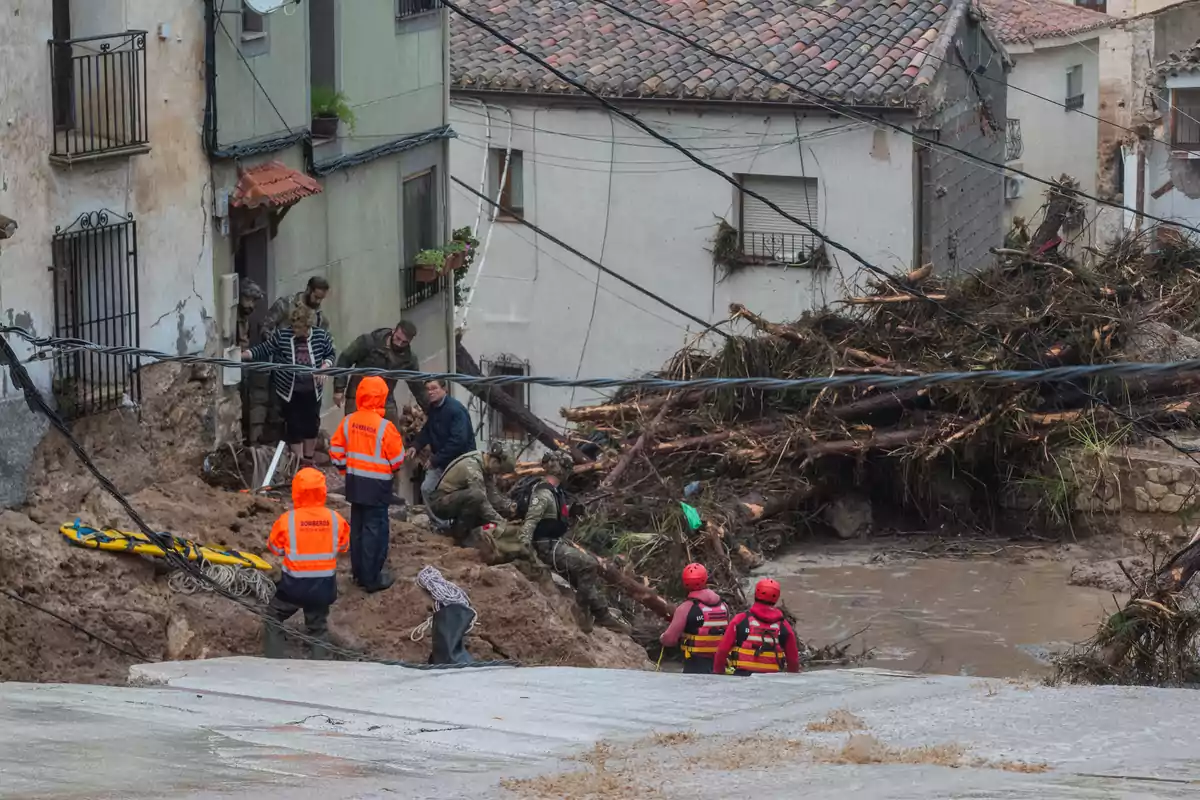 Personas con equipo de rescate trabajan en una zona afectada por un deslizamiento de tierra y escombros cerca de varias casas dañadas.