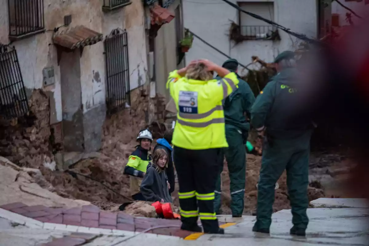 Un grupo de rescatistas y personal de emergencia asiste a una persona en una zona afectada por un deslizamiento de tierra frente a un edificio dañado.