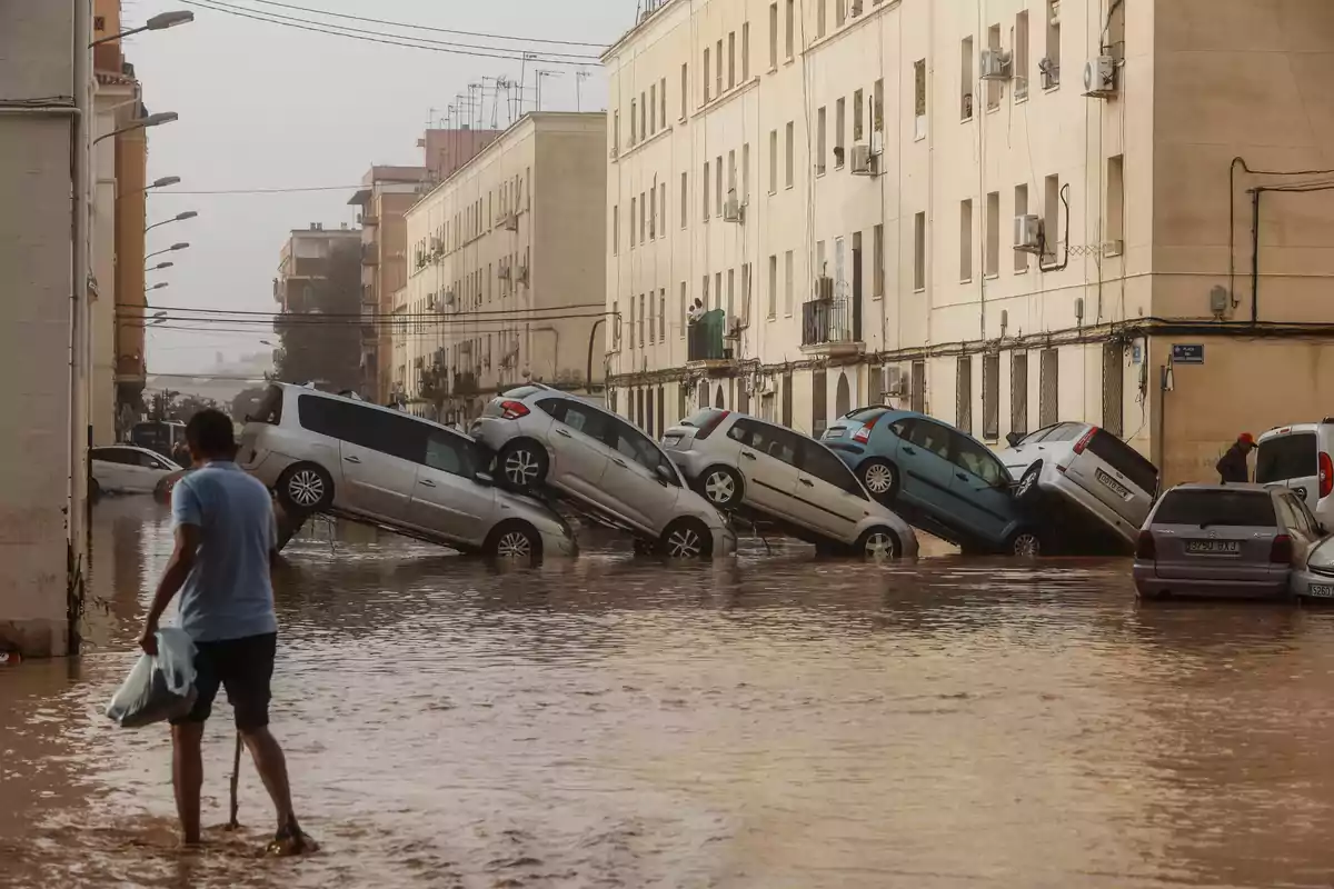 Una calle inundada con varios coches apilados unos sobre otros mientras una persona camina por el agua.