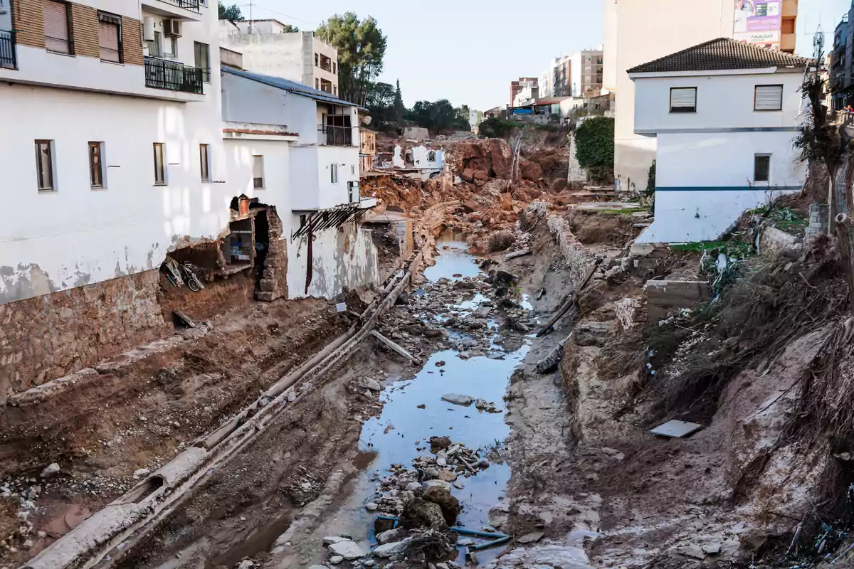 Edificios dañados junto a un cauce erosionado con escombros y agua estancada.