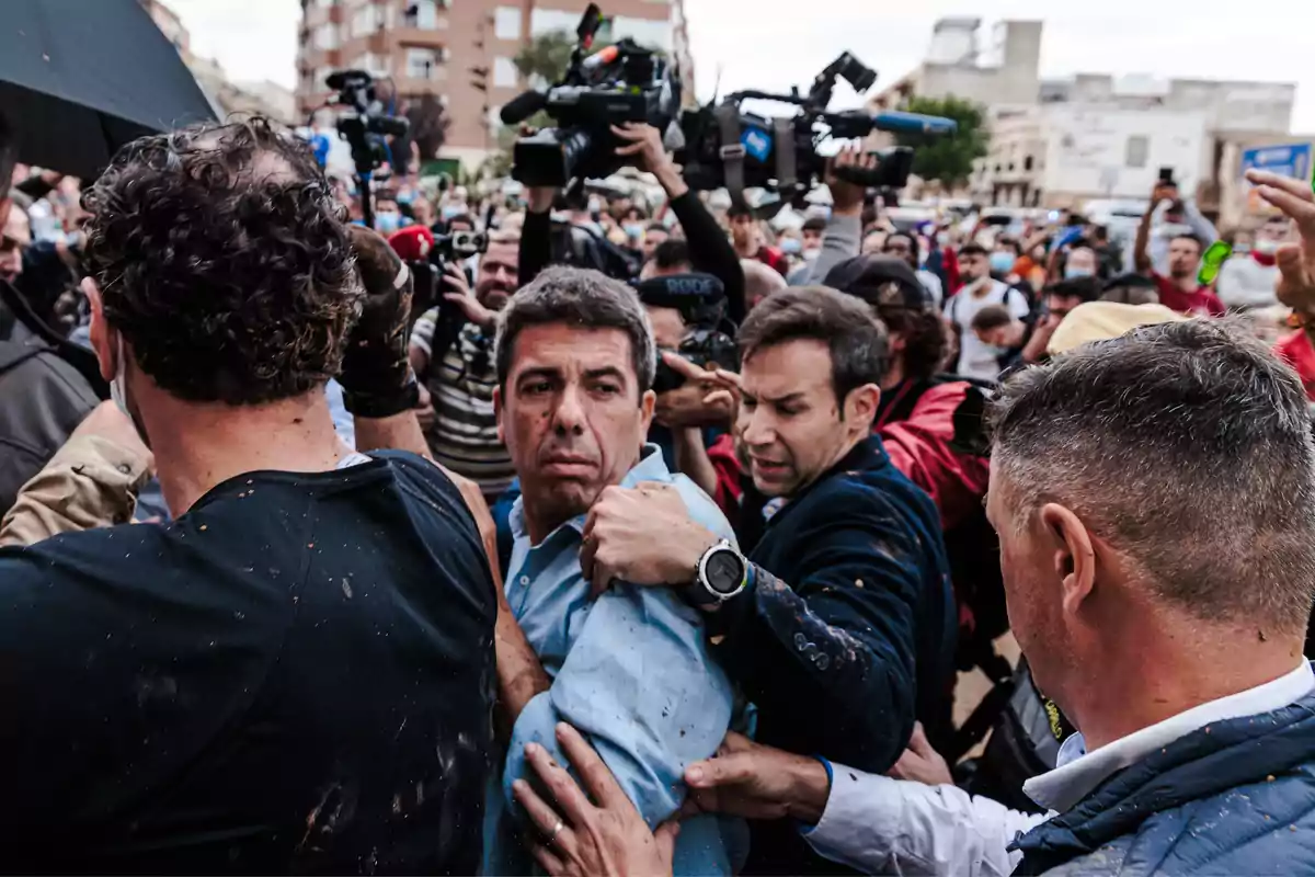 Una multitud de personas rodea a un hombre mientras varios camarógrafos y fotógrafos capturan el momento en un entorno urbano.