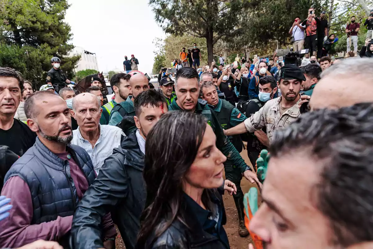 Un grupo de personas rodea a una mujer mientras la policía y la multitud observan en un entorno al aire libre.