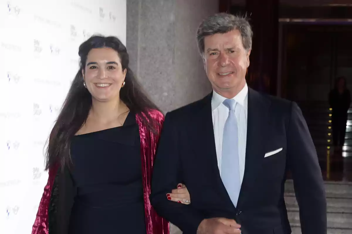 Una mujer y un hombre elegantemente vestidos posan sonrientes en un evento formal