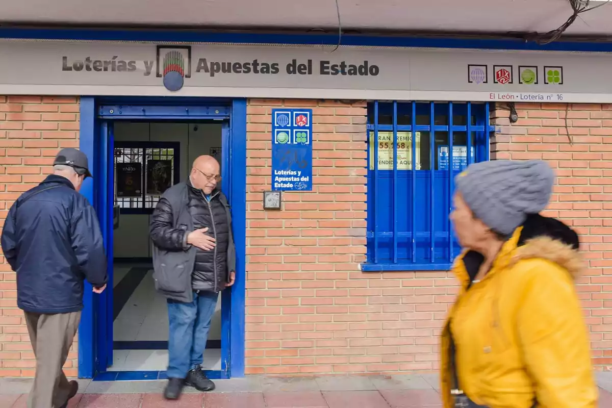 Una persona sale de una oficina de Loterías y Apuestas del Estado mientras otra persona pasa caminando frente al establecimiento.