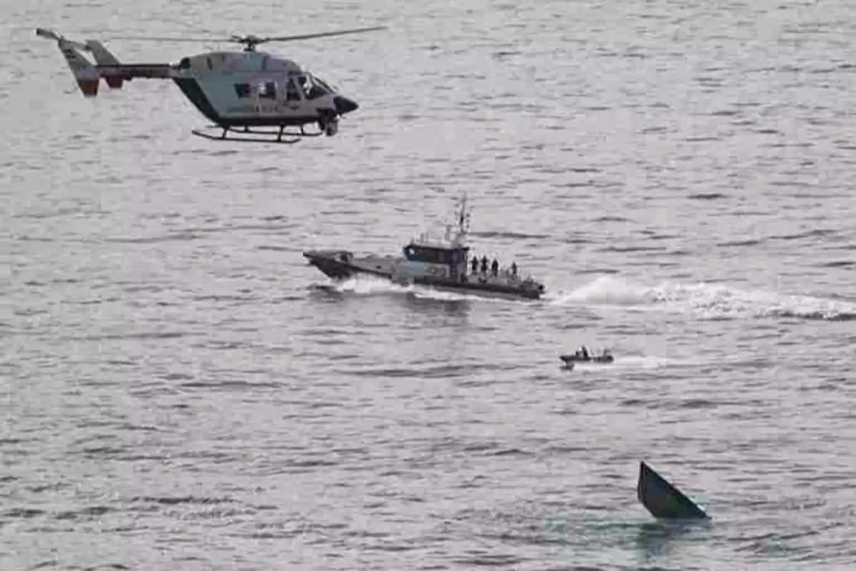 Un helicóptero y una lancha patrullera en el mar junto a una pequeña embarcación y un bote parcialmente hundido.