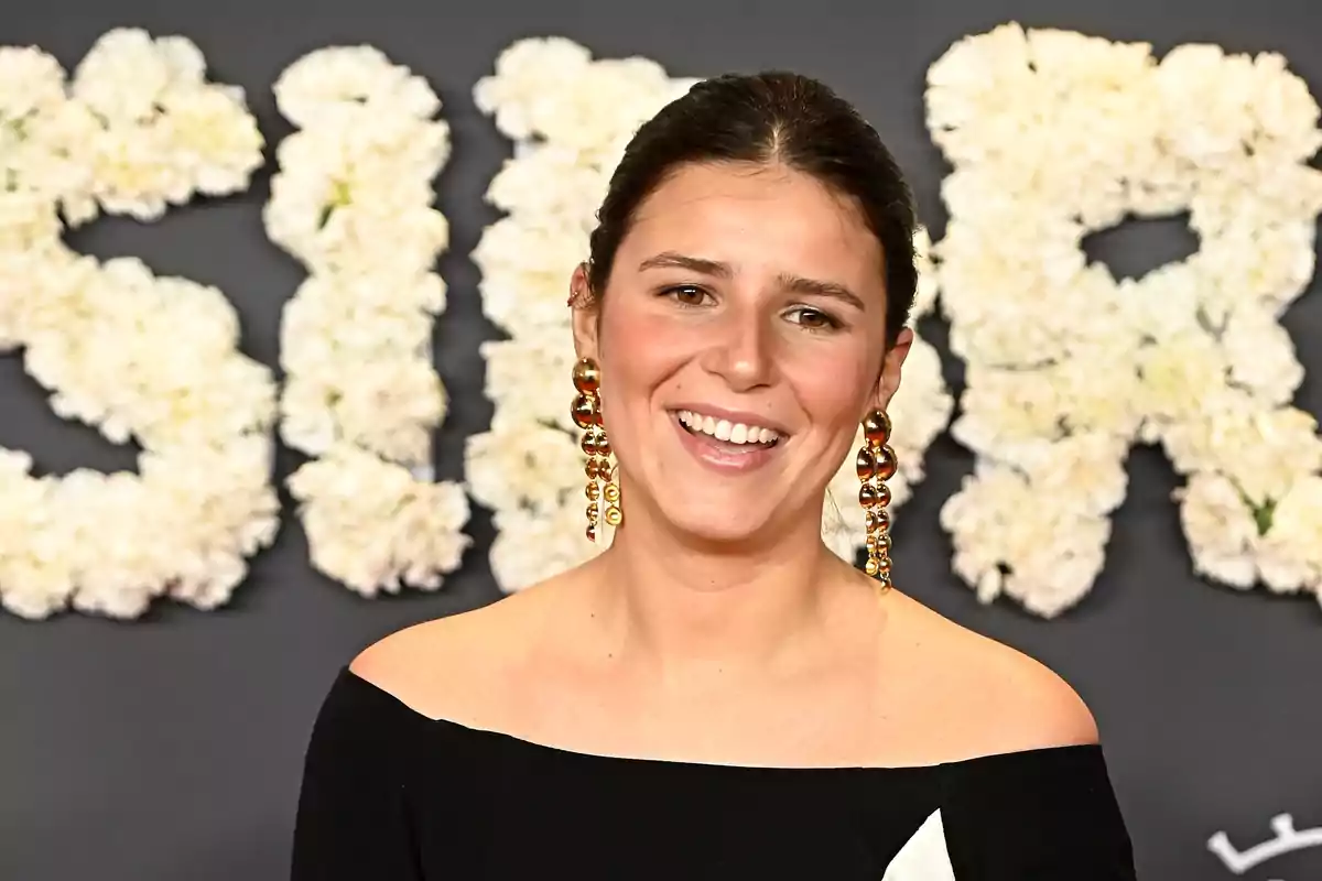Una persona sonriendo con un fondo de flores blancas que forman letras.