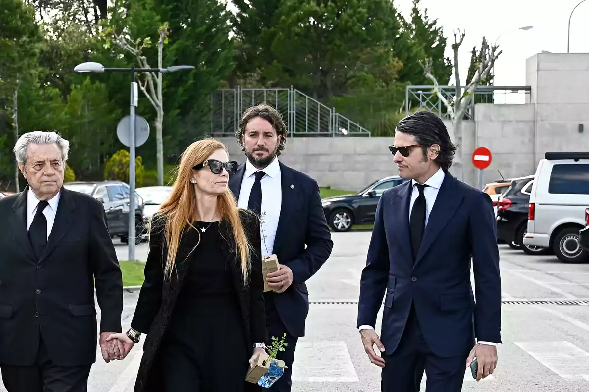 Un grupo de personas vestidas de negro camina por un estacionamiento, rodeado de árboles y vehículos. Un grupo de personas vestidas de negro camina por un estacionamiento, rodeado de árboles y vehículos.
