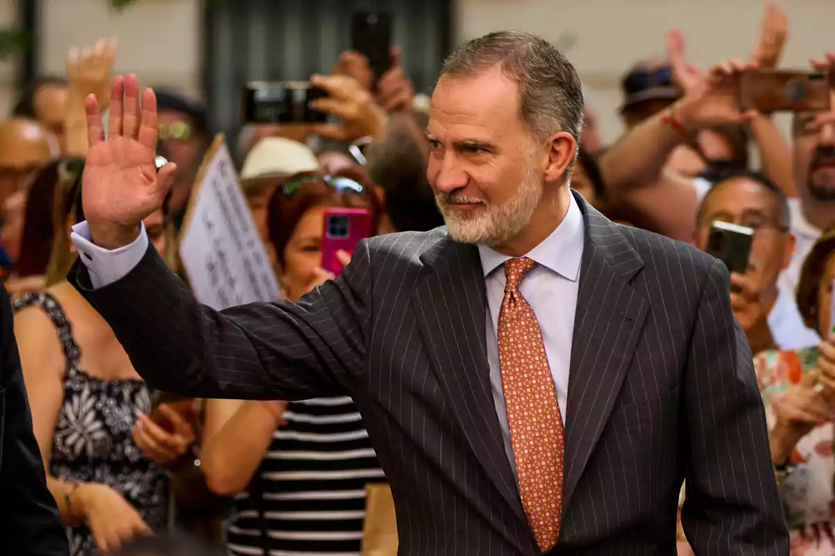 Hombre de traje a rayas saludando con la mano mientras una multitud lo observa y toma fotos Hombre de traje a rayas saludando con la mano mientras una multitud lo observa y toma fotos
