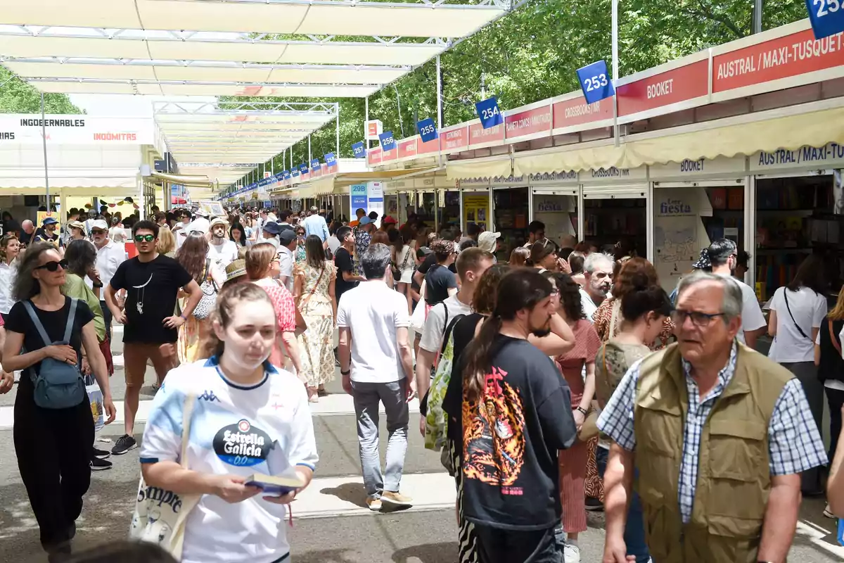 Personas caminando y visitando puestos de libros en una feria al aire libre en un día soleado Personas caminando y visitando puestos de libros en una feria al aire libre en un día soleado