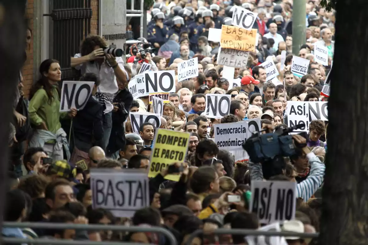 Una multitud de personas participa en una manifestación sosteniendo pancartas con mensajes de protesta.