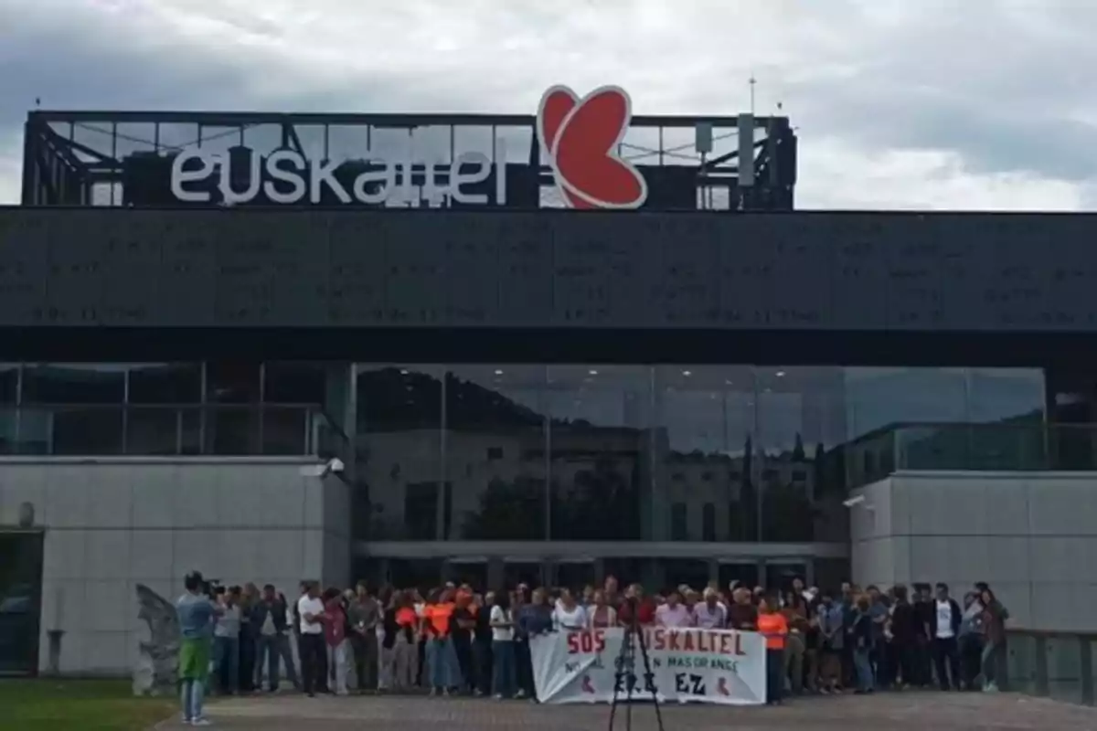 Un grupo de personas se manifiesta frente a un edificio con el logo de Euskaltel, sosteniendo una pancarta que dice "SOS EUSKALTEL NO MÁS EN MAS ORANGE EZ".