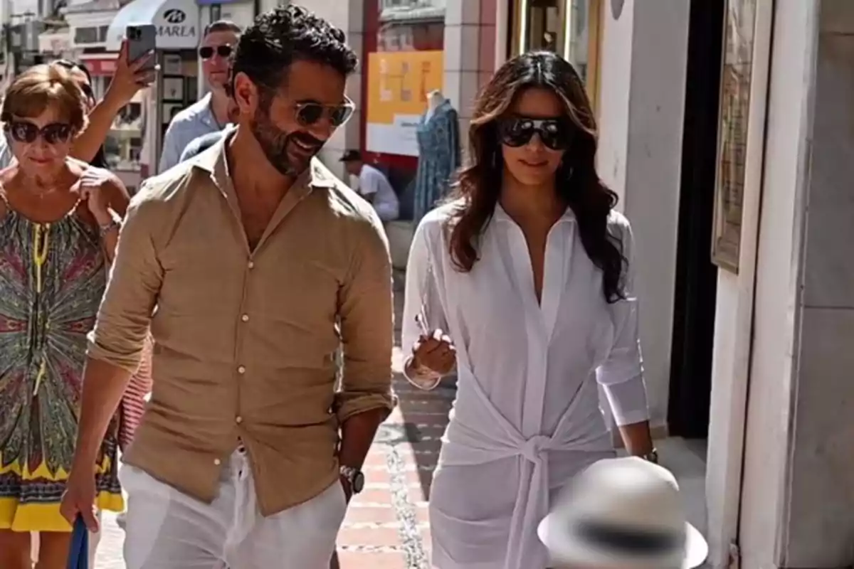 Pareja caminando por una calle soleada mientras sonríen y usan gafas de sol