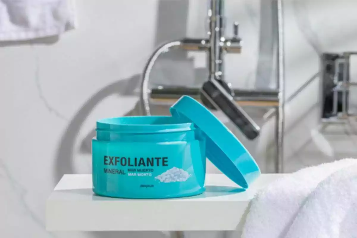 Envase azul de exfoliante mineral sobre una repisa en un baño con grifo de fondo. Envase azul de exfoliante mineral sobre una repisa en un baño con grifo de fondo.