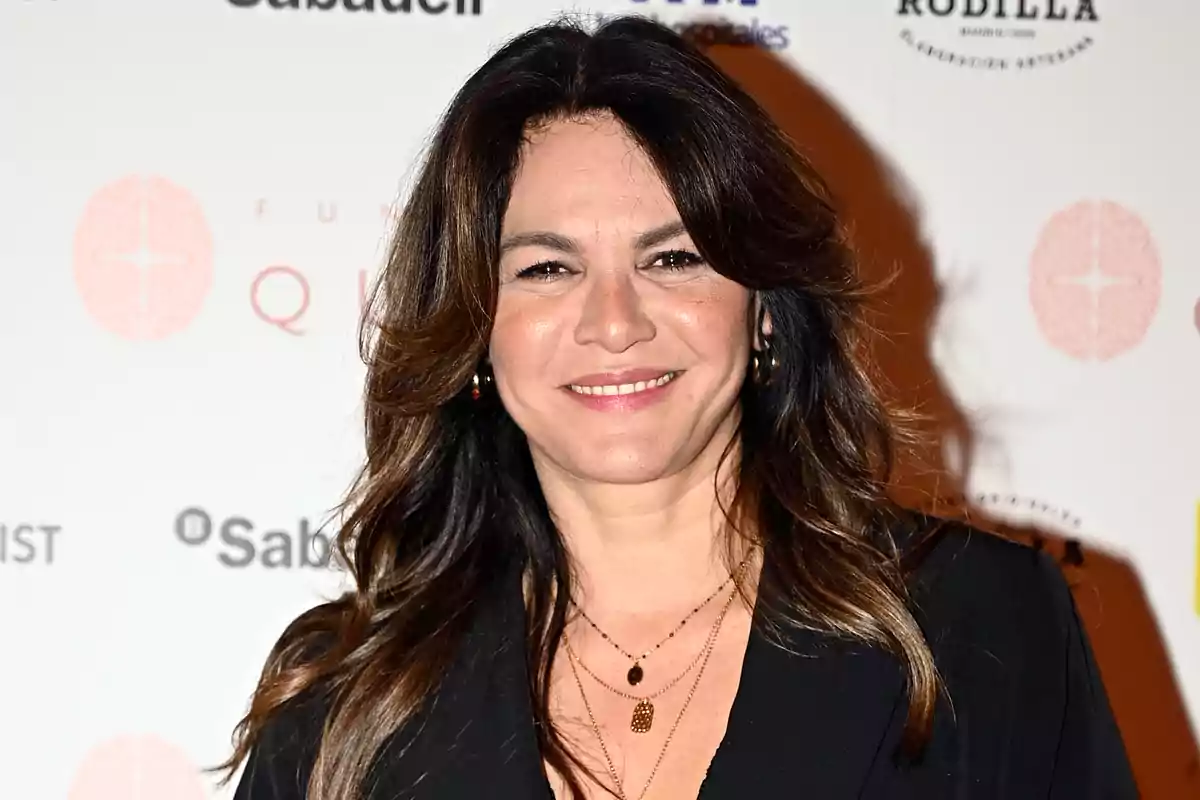 Fabiola Martínez, vestida de negro y sonriendo frente a un fondo con logotipos de marcas. Fabiola Martínez, vestida de negro y sonriendo frente a un fondo con logotipos de marcas.