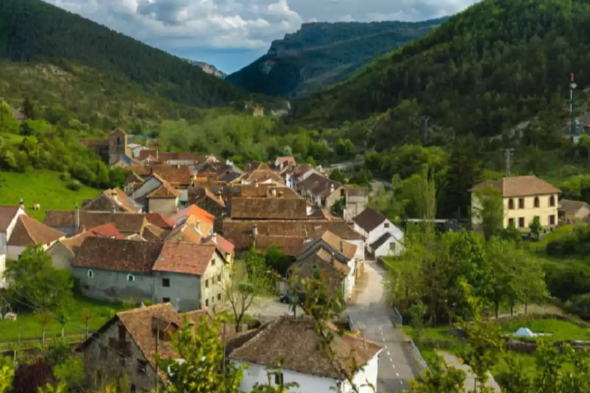 Vista panorámica de un pintoresco pueblo rodeado de montañas y vegetación exuberante bajo un cielo parcialmente nublado.