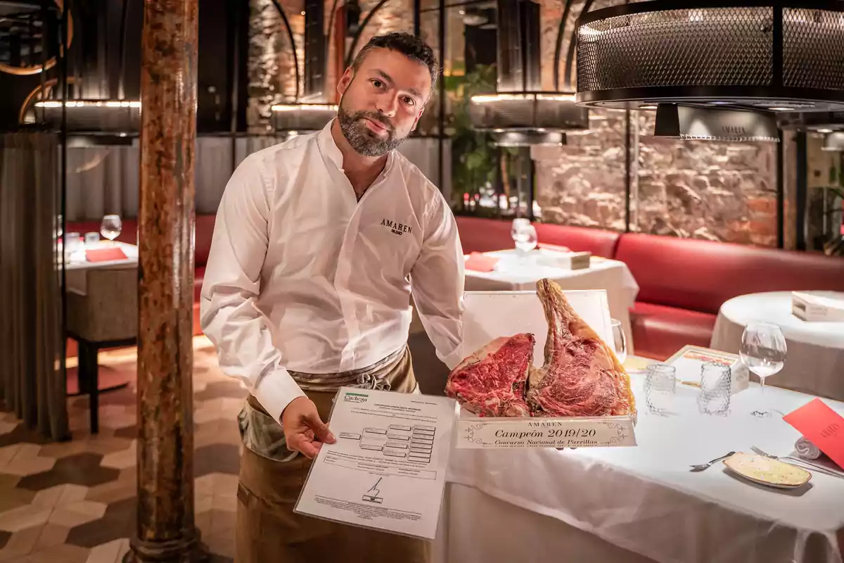 Un hombre con camisa blanca muestra un corte de carne y un documento en un restaurante elegante.