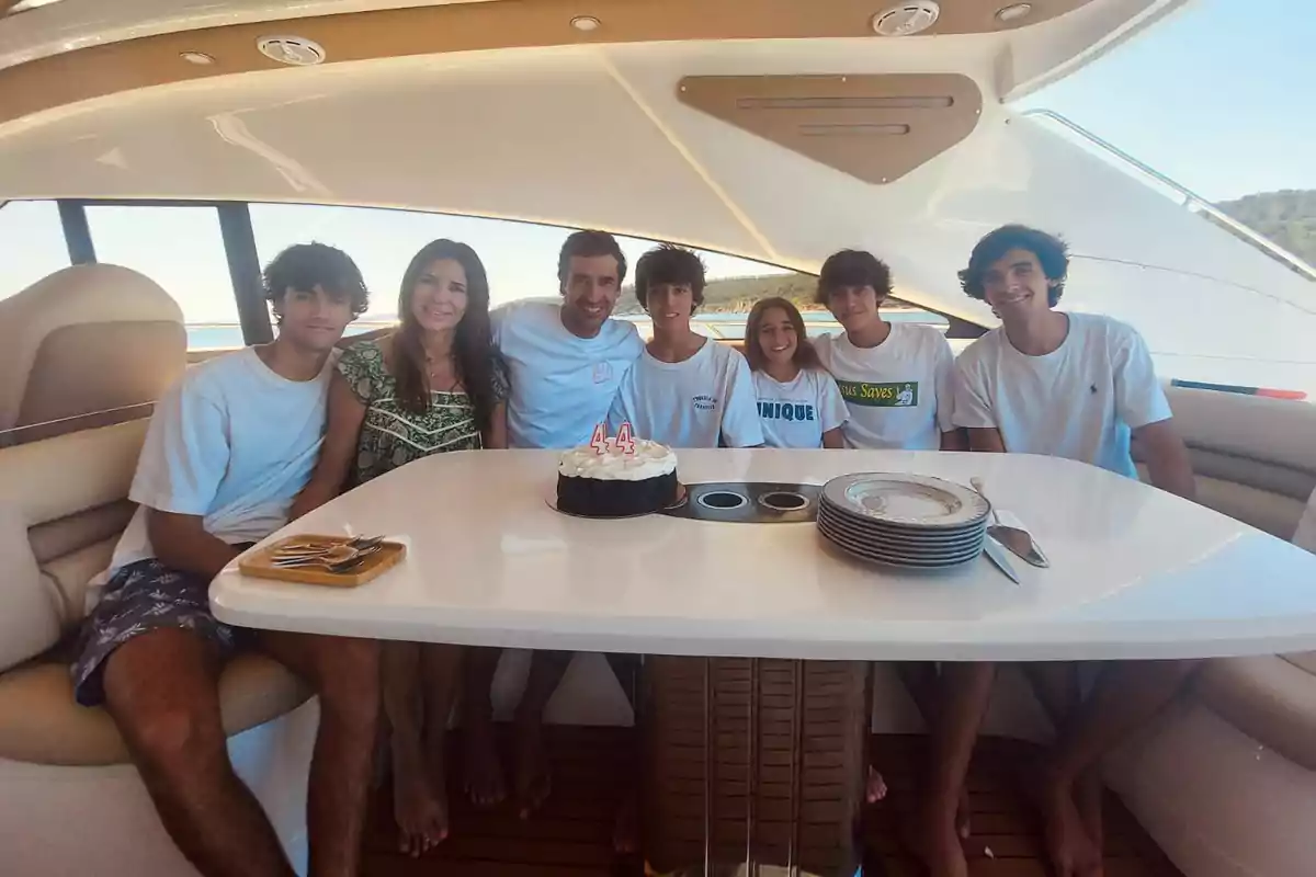 Un grupo de personas sentadas alrededor de una mesa en un yate con un pastel de cumpleaños en el centro.