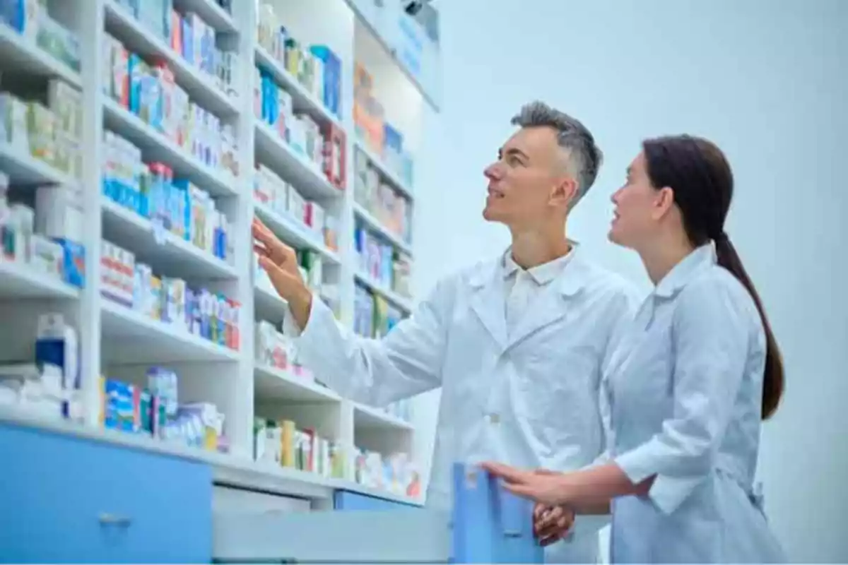 Dos farmacéuticos revisando estantes llenos de medicamentos en una farmacia.
