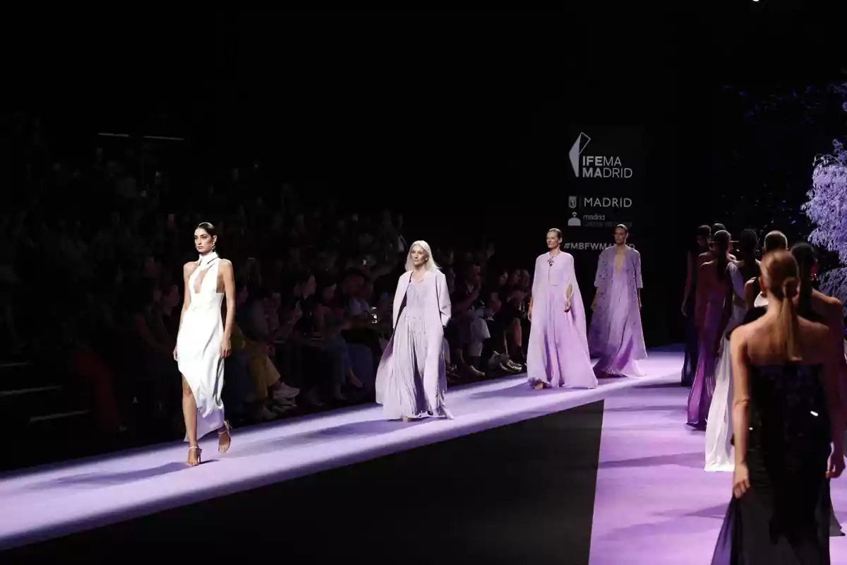 Modelos desfilando en una pasarela con vestidos en tonos lilas y blancos durante un evento de moda en IFEMA Madrid.