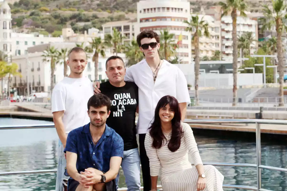 Un grupo de cinco personas posando frente a un puerto con edificios y palmeras al fondo.