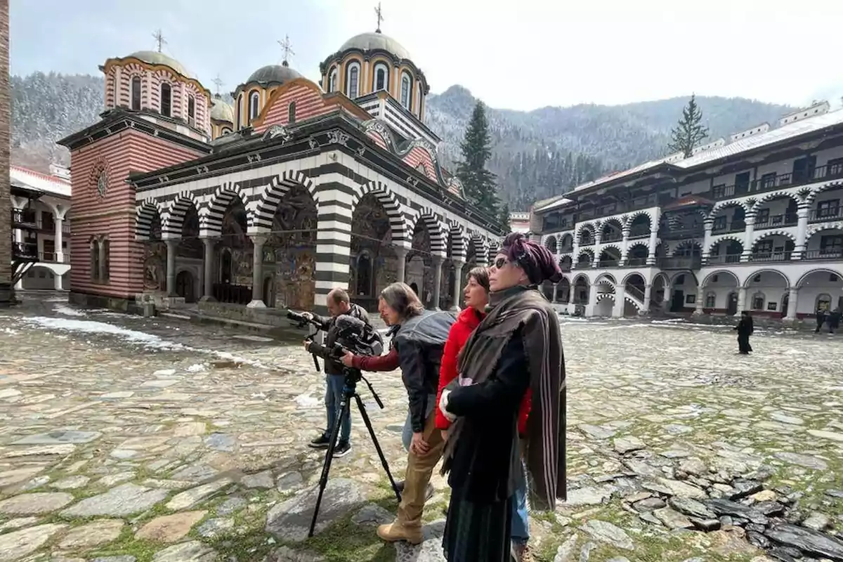 Un grupo de personas observa y filma un monasterio con arquitectura distintiva en un entorno montañoso.