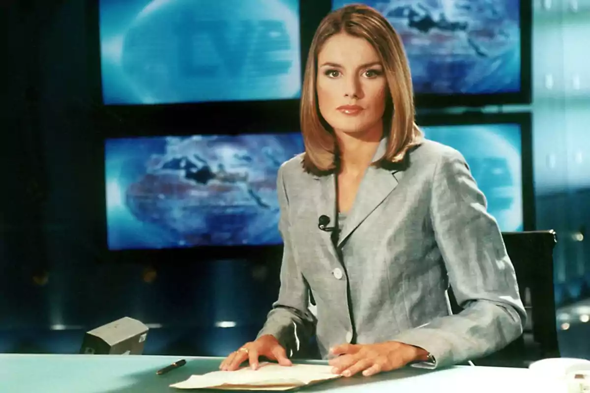 Presentadora de noticias en un estudio de televisión con pantallas de fondo mostrando un mapa del mundo.