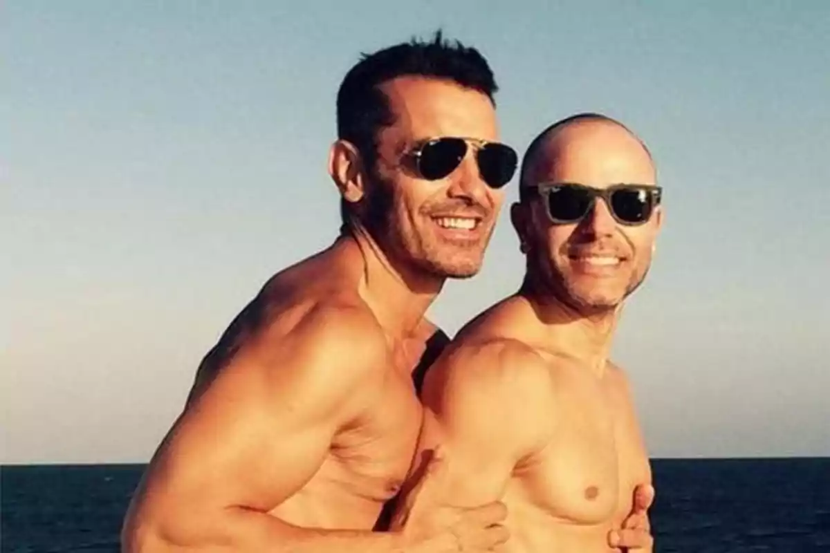 Dos hombres sonrientes posan abrazados en la playa usando gafas de sol Dos hombres sonrientes posan abrazados en la playa usando gafas de sol