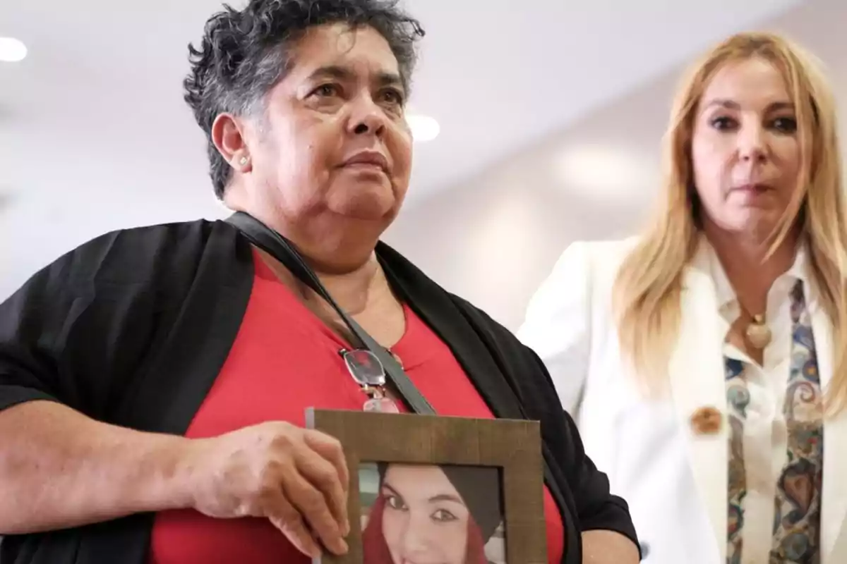 Dos mujeres, una de ellas sosteniendo un marco con una foto de una joven.