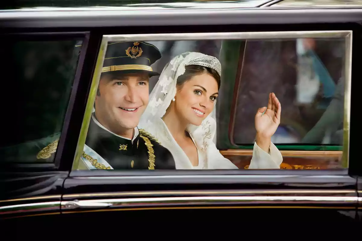 Felipe and Letizia dressed as bride and groom inside a vintage car, smiling and waving through the window. Still from 'Felipe y Letizia'