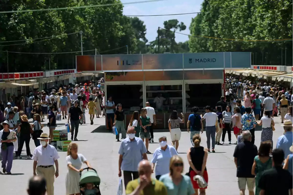 Una multitud de personas pasea por una feria de libros al aire libre en Madrid, rodeada de árboles y puestos de venta.