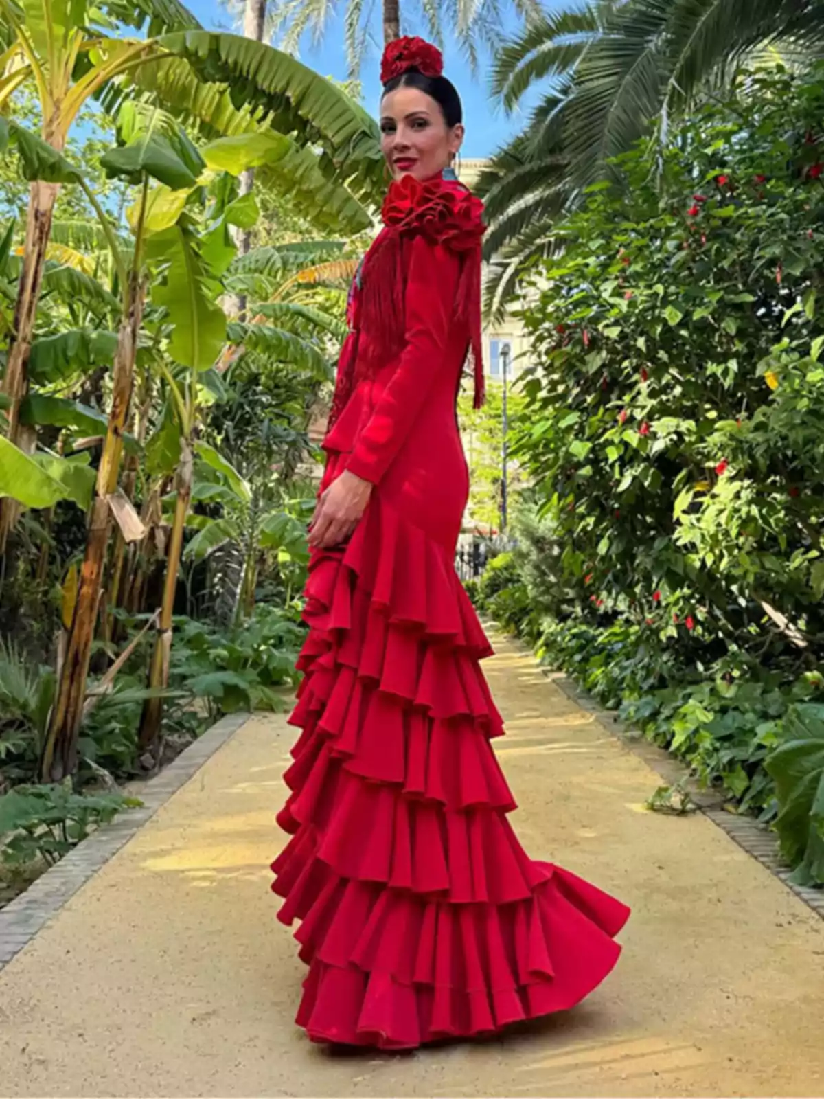Una mujer con un vestido rojo de volantes posa en un jardín tropical.
