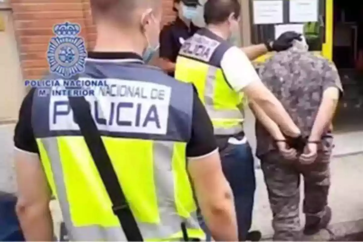 Agentes de la policía nacional escoltan a una persona esposada hacia un edificio Agentes de la policía nacional escoltan a una persona esposada hacia un edificio