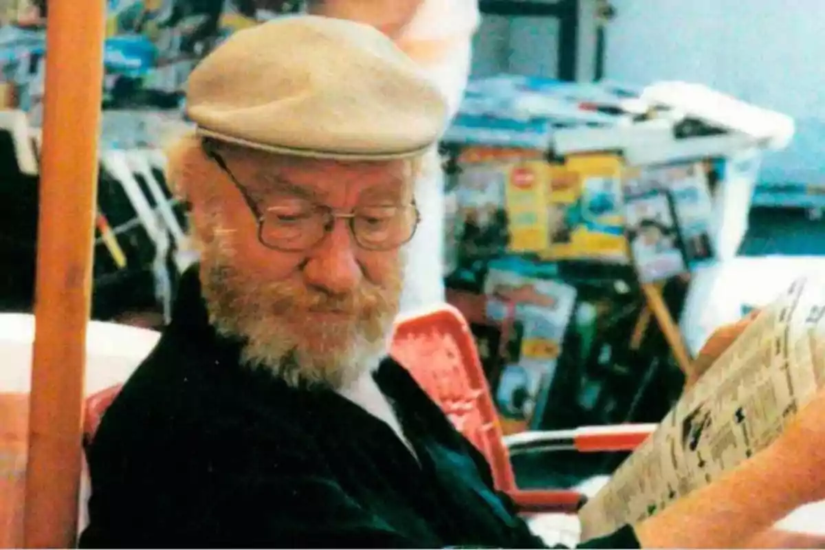 Hombre mayor con barba y gafas leyendo un periódico sentado en una silla roja Hombre mayor con barba y gafas leyendo un periódico sentado en una silla roja
