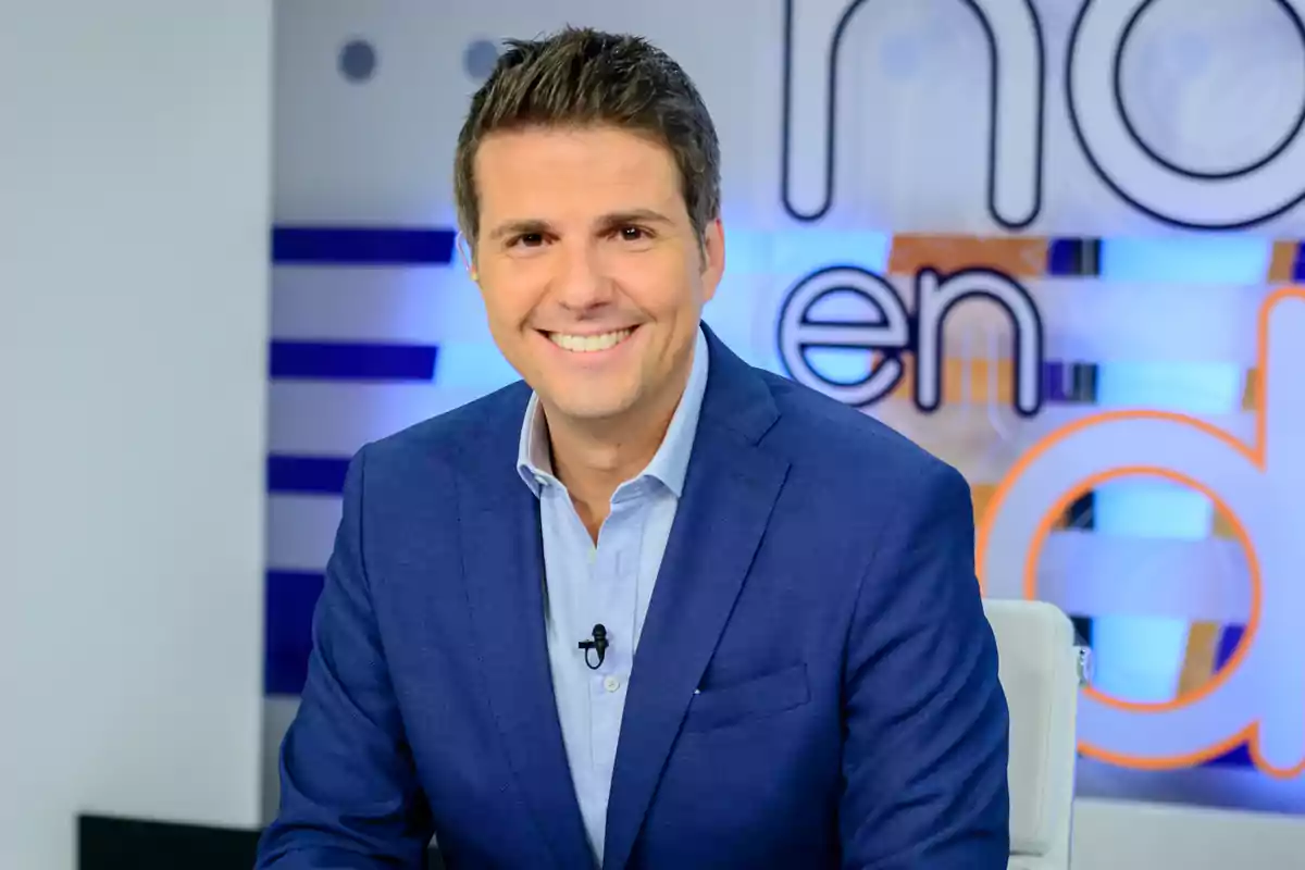 Un hombre sonriente con traje azul en un estudio de televisión.