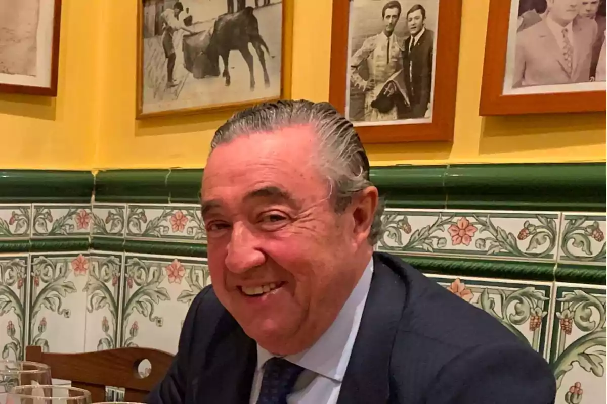 Un hombre sonriendo en un restaurante con azulejos decorativos y fotos en la pared.