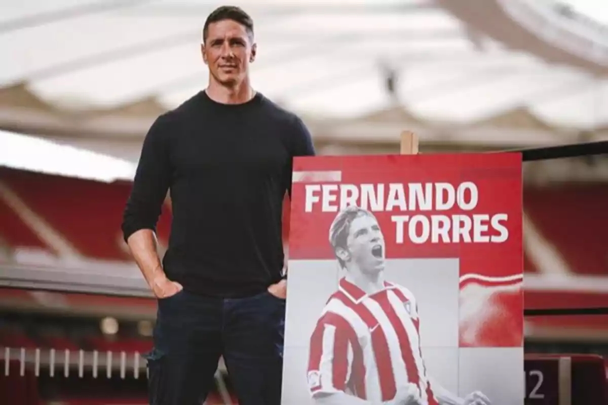 Un hombre de pie junto a un cartel con una imagen de un futbolista en un estadio.