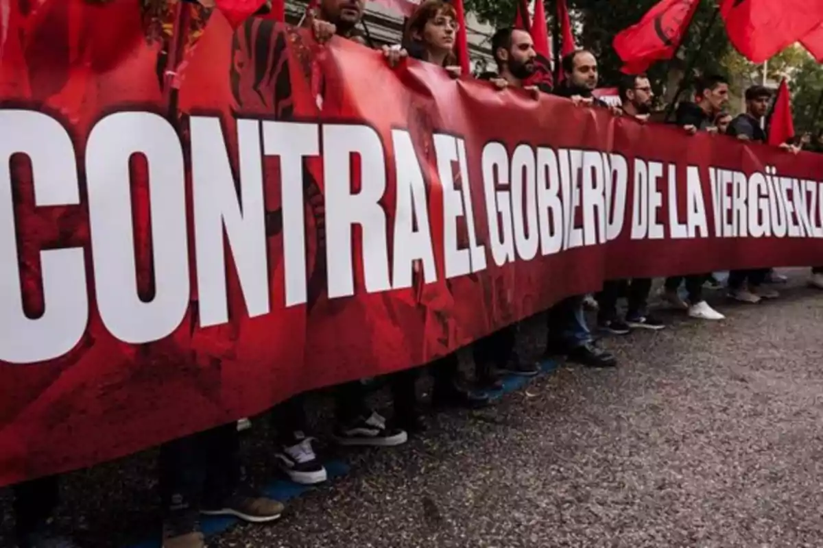 Un grupo de personas sostiene una pancarta roja con un mensaje de protesta.