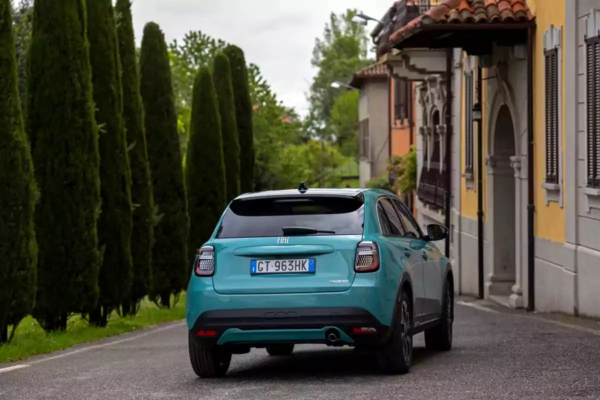 Un FIAT 600 Hybrid azul estacionado en una calle estrecha rodeada de árboles y edificios.