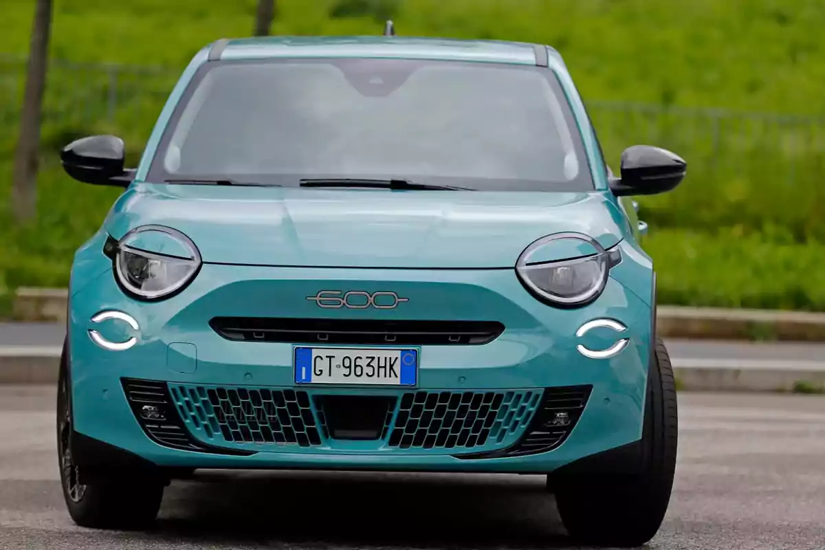 Un FIAT 600 Hybrid compacto azul estacionado en una carretera con fondo verde.